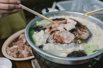closeup hand holding chopsticks picking up grilled pork from pan, thai style pork barbecue. Moo Kratha similar Yakiniku barbecue in japan ,we cooked on hot brass BBQ pan.