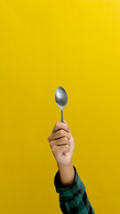 Hand Holding a Silver Stainless Steel Spoon, Isolated on a Yellow Background