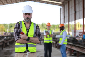 A senior civil engineer is seen from behind while working at a construction site. They are holding a walkie-talkie and overseeing the work progress.