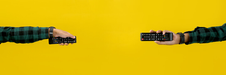 Hand Holding a Black TV Remote, Isolated on a Yellow Background