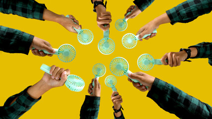 Hand holding small portable fan on isolated yellow background