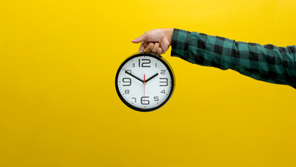 Hand holding a wall clock against a bright yellow background. Ideal for illustrating time...