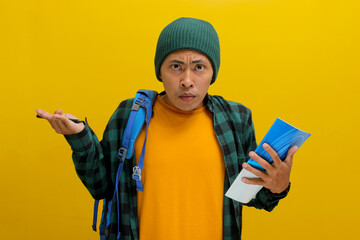 A confused young Asian student, dressed in a beanie hat and casual shirt and carrying a backpack,...