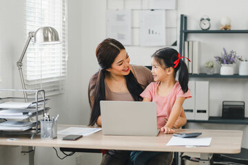 Smiling mother and daughter bonding while working with laptop in home office.