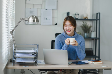 Smiling young woman enjoying a warm beverage during a break in a modern home office. Work life...