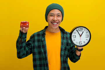 An Asian man, dressed in a beanie hat and casual shirt, holds a clock and a credit card, signaling...