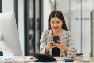 Smiling businesswoman checking smartphone at her modern office desk.