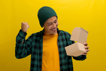 An excited Asian man, dressed in a beanie hat and casual shirt, eagerly unpacks the cardboard...