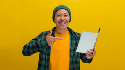 An excited young Asian student, dressed in a beanie hat and casual clothes, is pointing at a book...