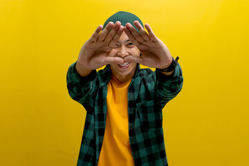 Young Asian man, dressed in a casual shirt and wearing a beanie hat, is creating a triangle shape...