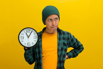 An uncertain Asian man, dressed in a beanie hat and casual shirt, holds a clock, appearing confused...