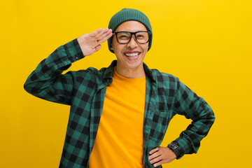 A young Asian man, dressed in a beanie hat and casual clothes, salutes with a cheerful expression...