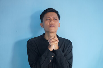 Handsome Asian young man wearing black shirt praying with hands together asking for forgiveness