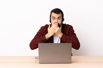 Telemarketer caucasian man working with a headset and with laptop covering mouth with hands.