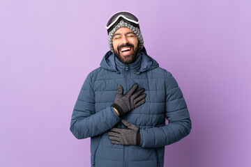 Skier man with snowboarding glasses over isolated purple background smiling a lot