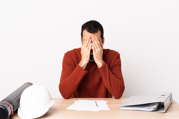 Caucasian architect man with beard in a table covering eyes by hands.