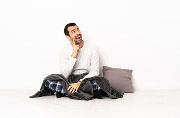 Caucasian man in pajamas sitting on the floor at indoors thinking an idea while looking up
