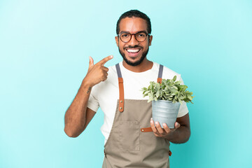 Gardener latin man holding a plant isolated on blue background giving a thumbs up gesture