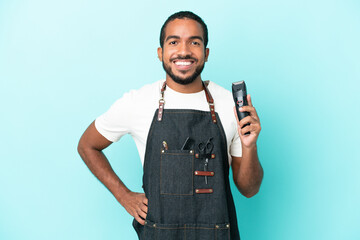Young hairdresser latin man isolated on blue background posing with arms at hip and smiling
