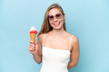 Young blonde woman in swimsuit holding an ice cream isolated on blue background smiling a lot
