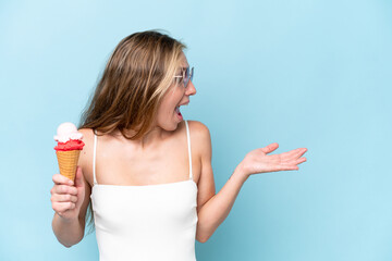 Young blonde woman in swimsuit holding an ice cream isolated on blue background with surprise...