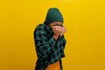 The amusingly frightened young Asian man hides his face with his shirt, expressing a mix of fear,...