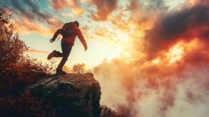 A person in hiking gear is stepping off a rock outcrop with autumn-colored vegetation around them. The sky is dramatic, filled with fiery clouds illuminated by the low sun, suggesting either sunrise o