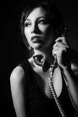 Black and white studio portrait of a caucasian woman in her 30s holding a vintage rotary phone and...