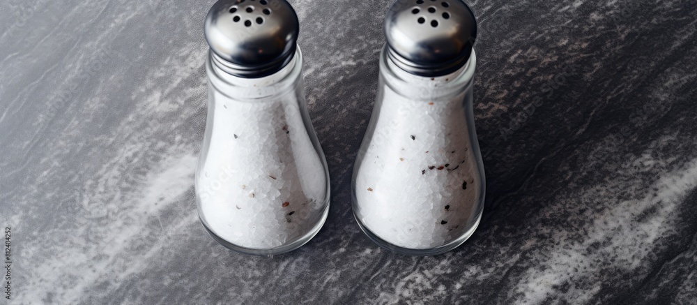 Poster top view of salt and pepper shakers placed on a textured grey table there is copy space available fo