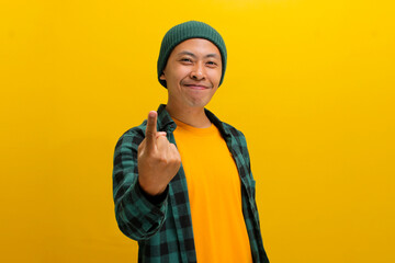 Happy, smiling young Asian man, dressed in a beanie hat and casual shirt, invites with a beckoning...