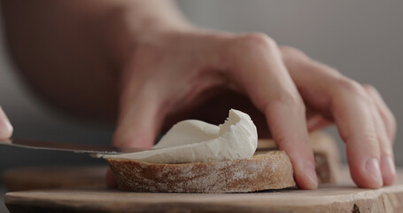 man hand spreading cream cheese on dark ciabatta