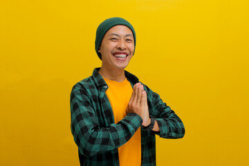 Joyful, smiling young Asian Muslim man, dressed in a beanie hat and casual shirt, gestures the Eid...