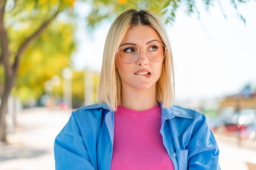 Young pretty woman with glasses at outdoors with confuse face expression