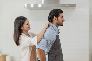 Happy couple cooking together in the kitchen at home, A couple wears apron to each other to make breakfast