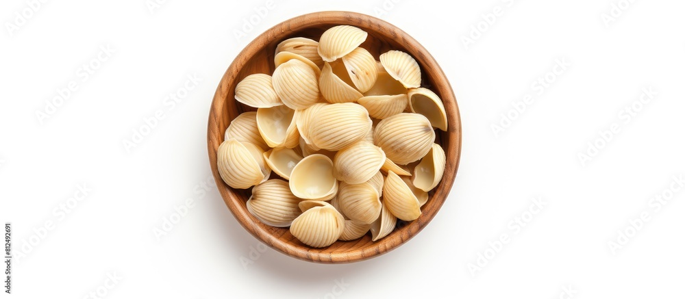 Poster Top view of a wooden bowl filled with raw striped shell pasta known as conchiglie rigate placed on a white background creating a perfect copy space image