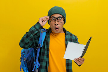 A shocked young Asian student, dressed in a beanie hat, casual clothes, eyeglasses, and carrying a...