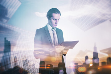 Attractive young european businessman with tablet standing on blurry airy city background with mock...