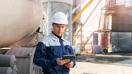 Industrial Worker man in hard hat uses tablet background of cement concrete mixer. Concept building...