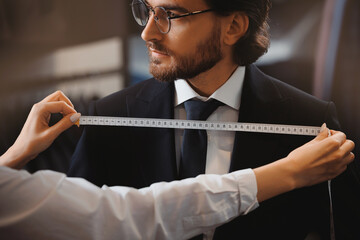 Professional dressmaker taking measurements of businessman in atelier classic menswear. Tailor...