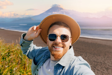 Selfie adventure photo, Happy young man tourist smiling in hat on black volcanic sand of Pacific...