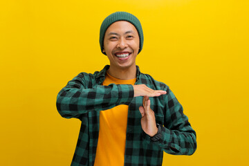 Enthusiastic Asian man in a beanie and casual clothes throws up a TIME OUT gesture with a playful smile, looking directly at the camera. Fun breaks, time management, or playful communication concept