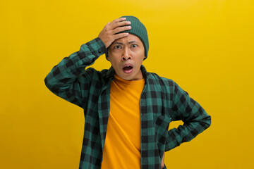 Troubled young Asian man, dressed in a beanie hat and casual shirt, is depicted holding his hand to...