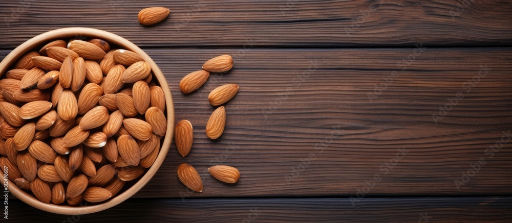 Poster a flat lay image shows almonds neatly arranged in a bowl while some are scattered on a wooden backgr