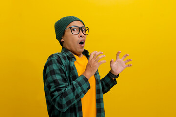 Thrilled Asian man in a beanie and casual shirt adjusts his glasses, eyes wide with surprise as he...