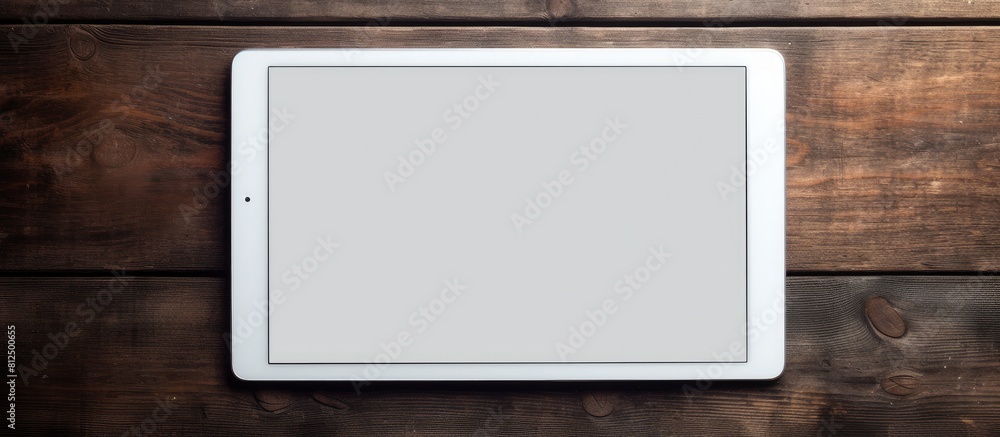 Poster a white digital tablet is placed on a dark wooden table creating a contrast in colors and textures. 