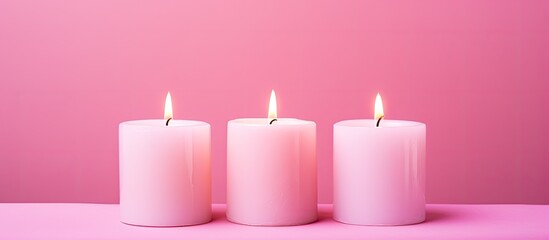A flat lay image features three white wax candles placed on a pink background leaving ample copy space
