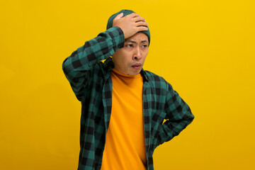 Young Asian man, dressed in a beanie hat and casual shirt, is holding his head, suggesting he's...