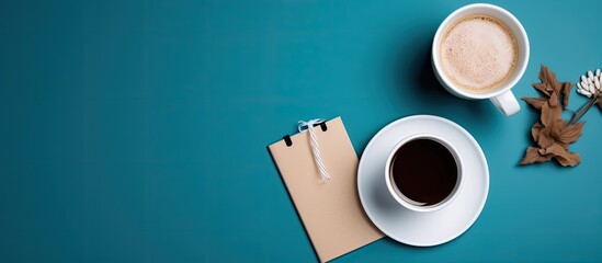 A cup of coffee sits alongside a gift box and a notebook with a pen all placed on a blue background The white paper displays the words Thank you These elements are captured in the copy space image