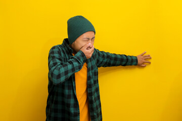 Young Asian man, wearing a beanie hat and casual shirt, appears to be suffering from a stomachache...