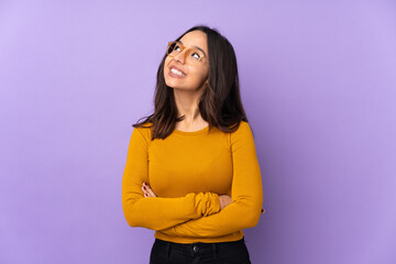 Young mixed race woman isolated on purple background looking up while smiling